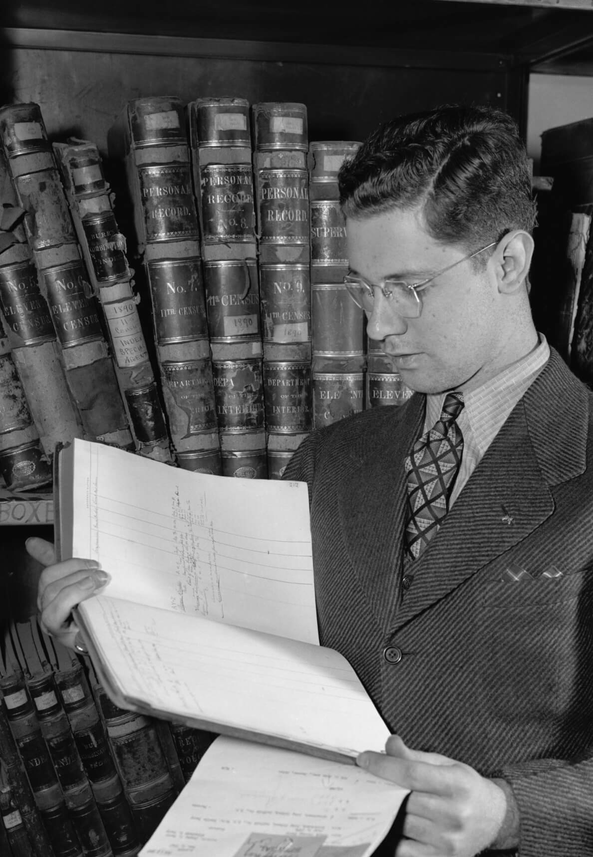 A young man in a suit standing and reading a book